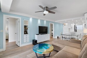 A modern living room with a ceiling fan, a glass coffee table, a sofa, and a TV on a white cabinet. - Royal Mauian, #511 2 Bedroom Condo by RedAwning (Kihei)