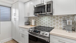 A modern kitchen with white cabinets, a stainless steel microwave, a built-in oven, and a stovetop. - Royal Mauian, #511 2 Bedroom Condo by RedAwning (Kihei)