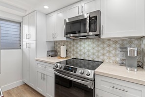 A modern kitchen with white cabinets, a stainless steel microwave, a built-in oven, and a stovetop. - Royal Mauian, #511 2 Bedroom Condo by RedAwning (Kihei)