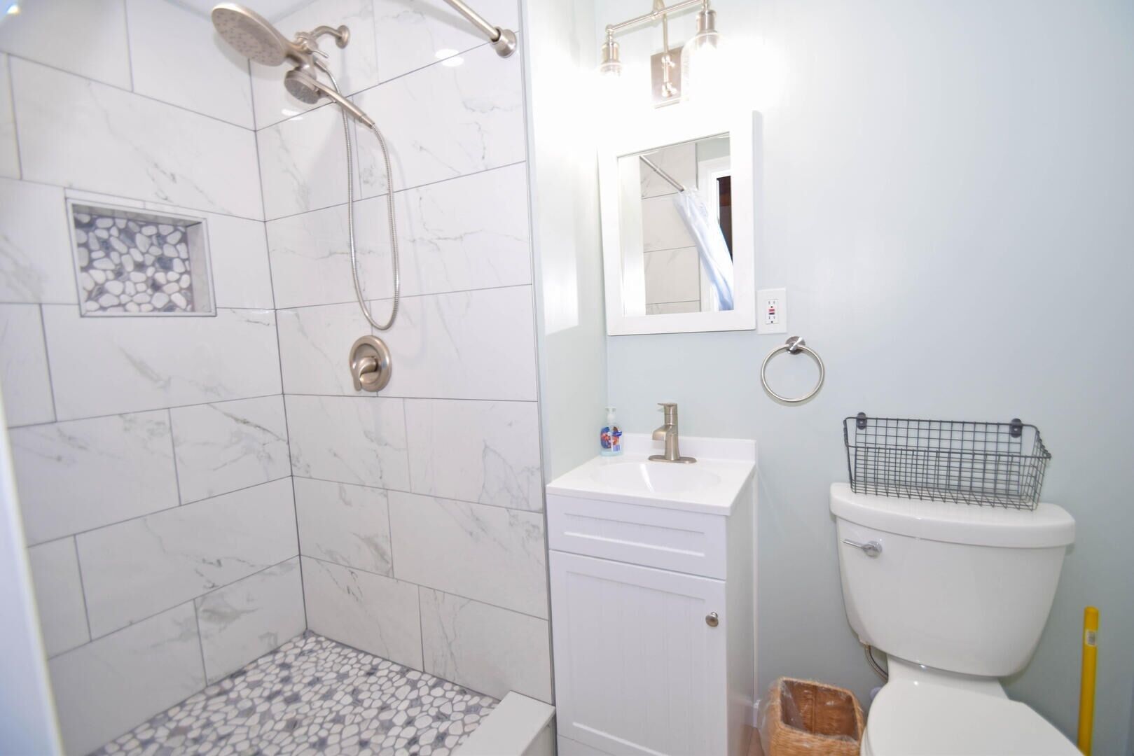 A bathroom with a shower, toilet, sink, and a small mirror.