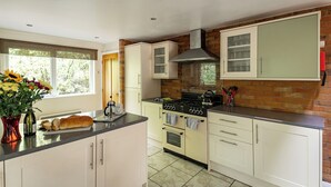Une cuisine avec des meubles blancs, une cuisinière à gaz et un mur en briques.