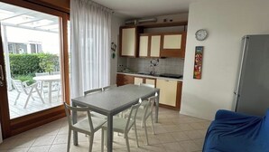 A compact kitchen with a dining table and chairs, a refrigerator, and a clock on the wall.