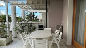 A covered patio area with a white table and chairs, surrounded by potted plants and a view of the cityscape.