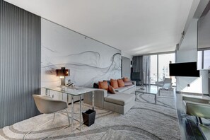 Een moderne hotelkamer met een glazen bureau, een bank met kussens, een flatscreen televisie en een groot raam met uitzicht op de stad.