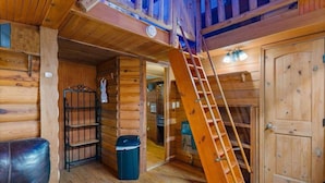 A wooden cabin interior with a wooden staircase, a metal shelf, a trash bin, and a door. - Beautiful Cabin in a great neighborhood and minutes from Baton Rouge!! (Denham Springs)