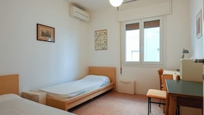A small, well-lit room with two single beds, a desk, and a chair. - VILLA MARGHERITA 1 (Lido di Jesolo)