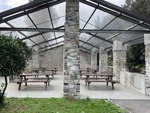 A covered outdoor area with stone pillars, wooden benches, and a glass roof. - Sea And Park-genoa Nervi - (Genoa)