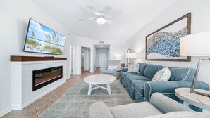 A living room with a fireplace, a television, a ceiling fan, and a large window. - Beachfront, Updated!  1BR (Orange Beach)