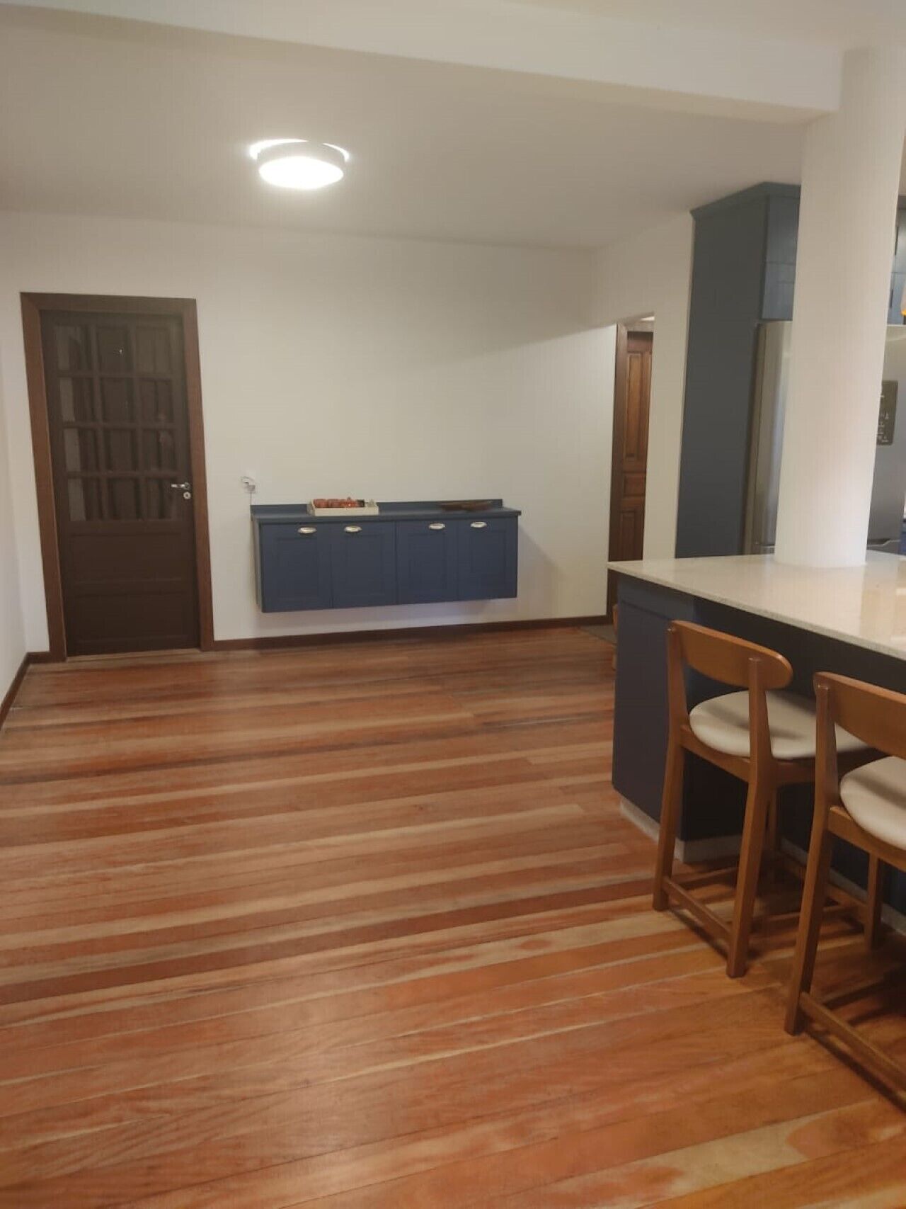 A kitchen with wooden flooring, a blue cabinet, and two wooden chairs.