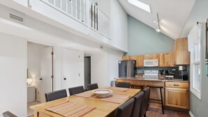 Eine moderne Küche mit Holzausstattung, einer Mikrowelle und einem Kühlschrank. Es gibt einen Essbereich mit Tisch und Stühlen sowie einen Balkon mit Geländer.