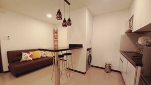 A compact living space with a kitchenette, a washing machine, a dining area with a bar stool, and a sofa with cushions. - Buena Vista Rental House (Santa Cruz)