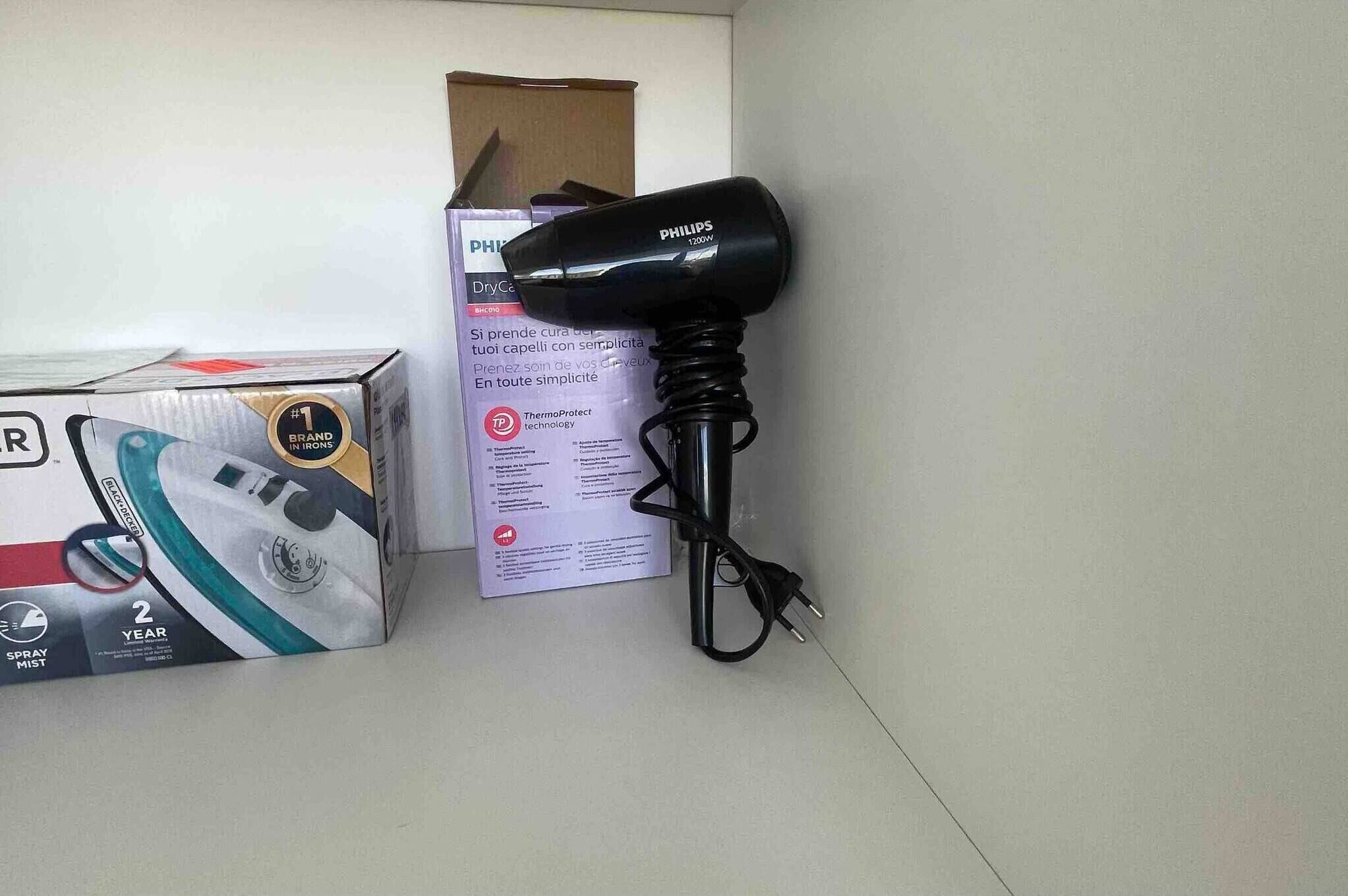 Un secador Philips, un aerosol y una caja sobre una superficie plana.