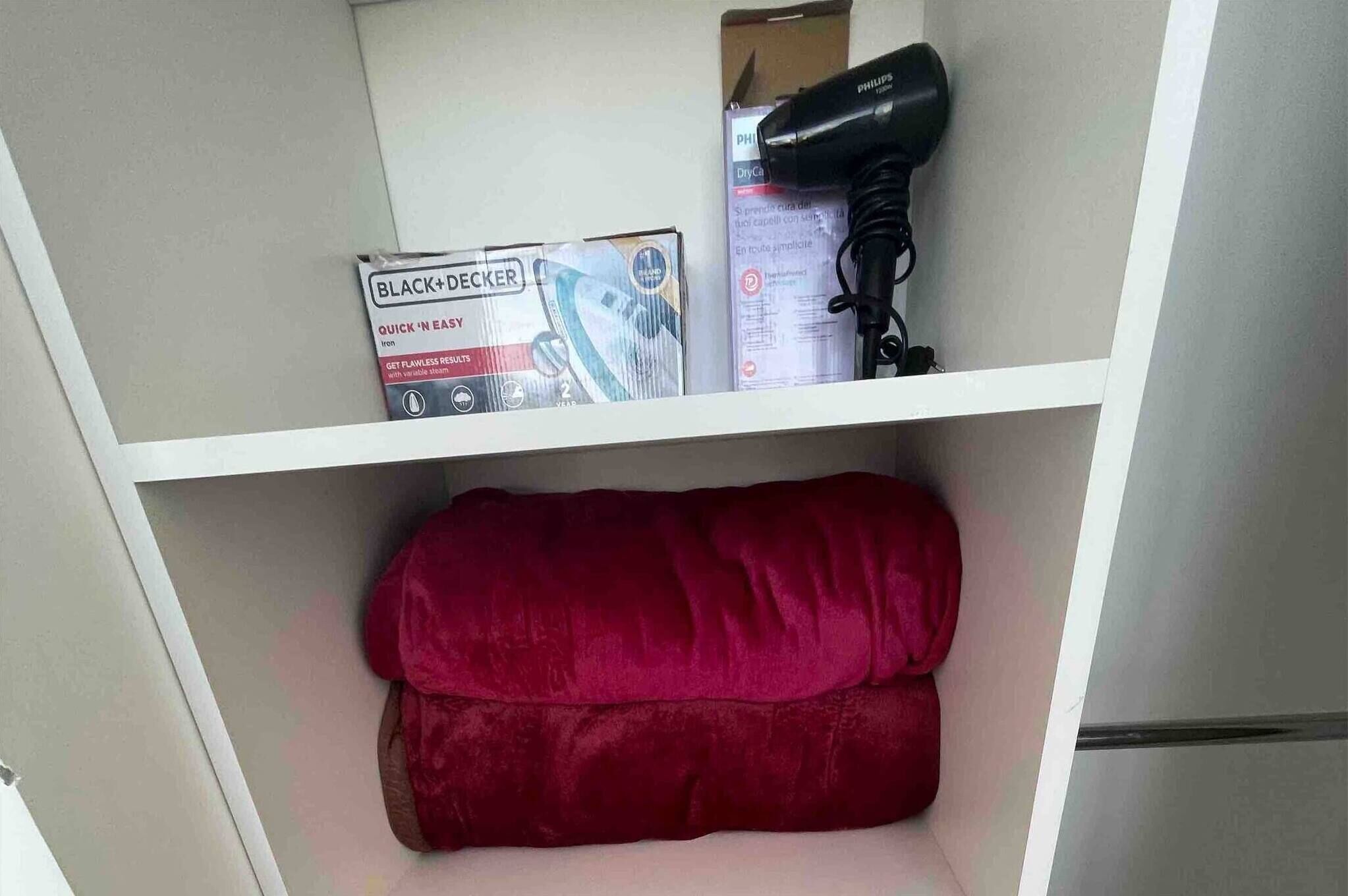 A shelf with a box labeled "BLACK+DECKER," a hairdryer, and a red cushion.