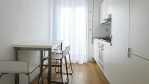 Una cocina pequeña y luminosa con armarios blancos, encimera de madera y una ventana con cortinas traslúcidas.