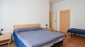 Habitación individual con una cama que tiene cabecera de madera, una mesita de noche con lámpara, un armario y un banco.