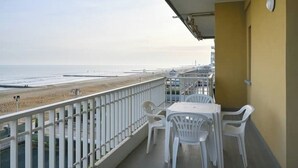 Un balcón con vistas a la playa, sillas de plástico blancas y una mesa.