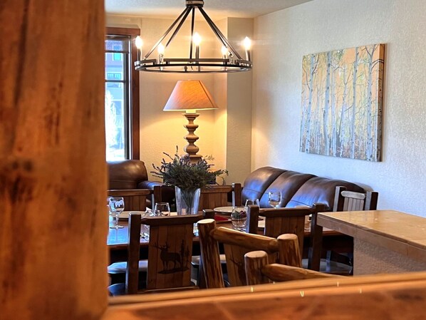 A dining area with a wooden table, chairs, a bench, a chandelier, a lamp, and a painting on the wall.