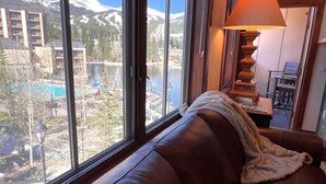 Ein Zimmer mit großem Fenster und Blick auf einen Berg, ein Schwimmbad und ein Gebäude.