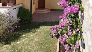 Un edificio a due piani con facciata gialla, un ingresso ben visibile e un piccolo giardino con fiori viola.