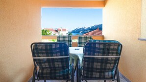 Un balcone con due sedie a quadri e un tavolo, con vista su un paesaggio montuoso e un corpo d'acqua.