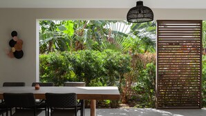 Un coin repas avec une table et des chaises en bois, une plante en pot et une vue sur une végétation luxuriante par la fenêtre.