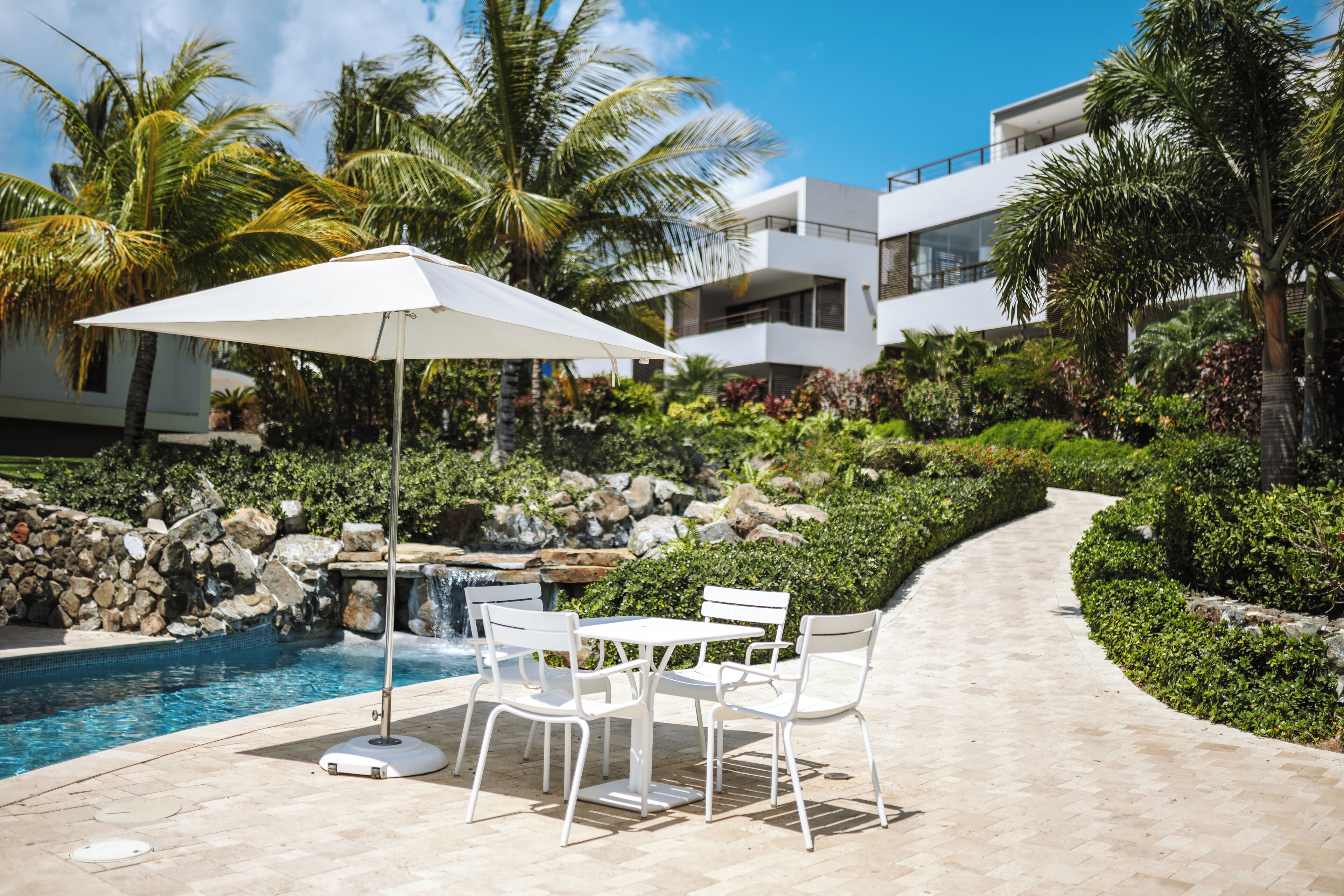 A pool area with a table and chairs, surrounded by palm trees and a modern building.