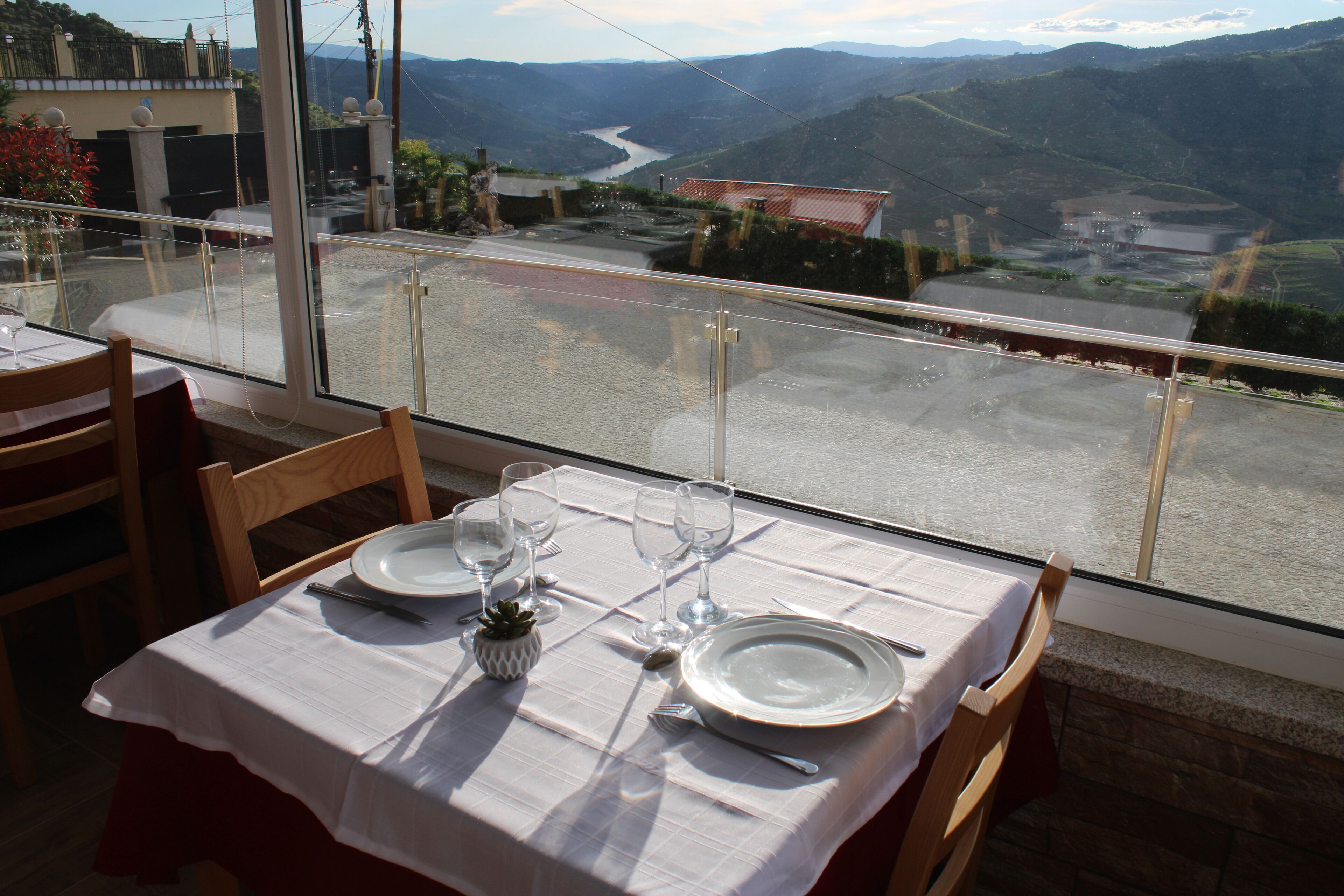 A dining table set with plates, glasses, and cutlery, overlooking a scenic valley.