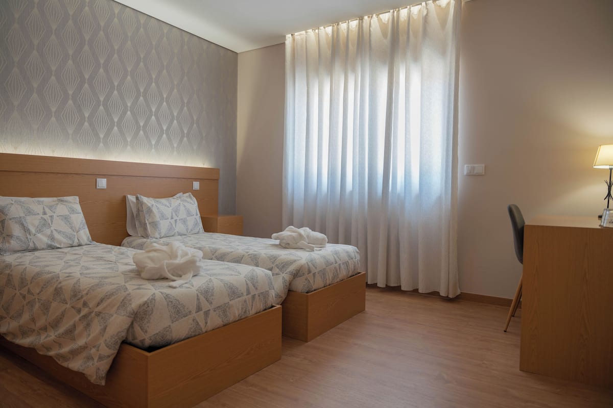 A hotel room with two beds, a desk, and a large window with curtains.