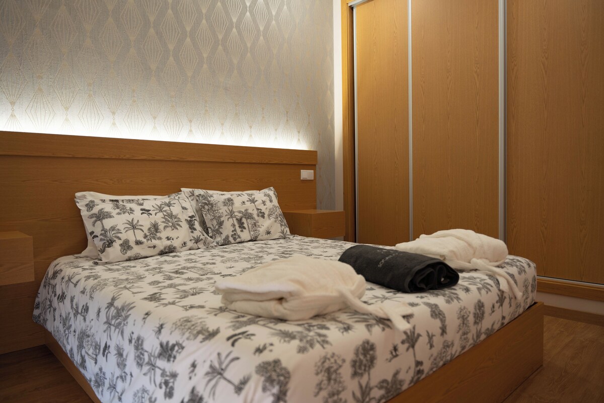 A neatly made bed with floral-patterned bedding, a bedside table, and a wardrobe.