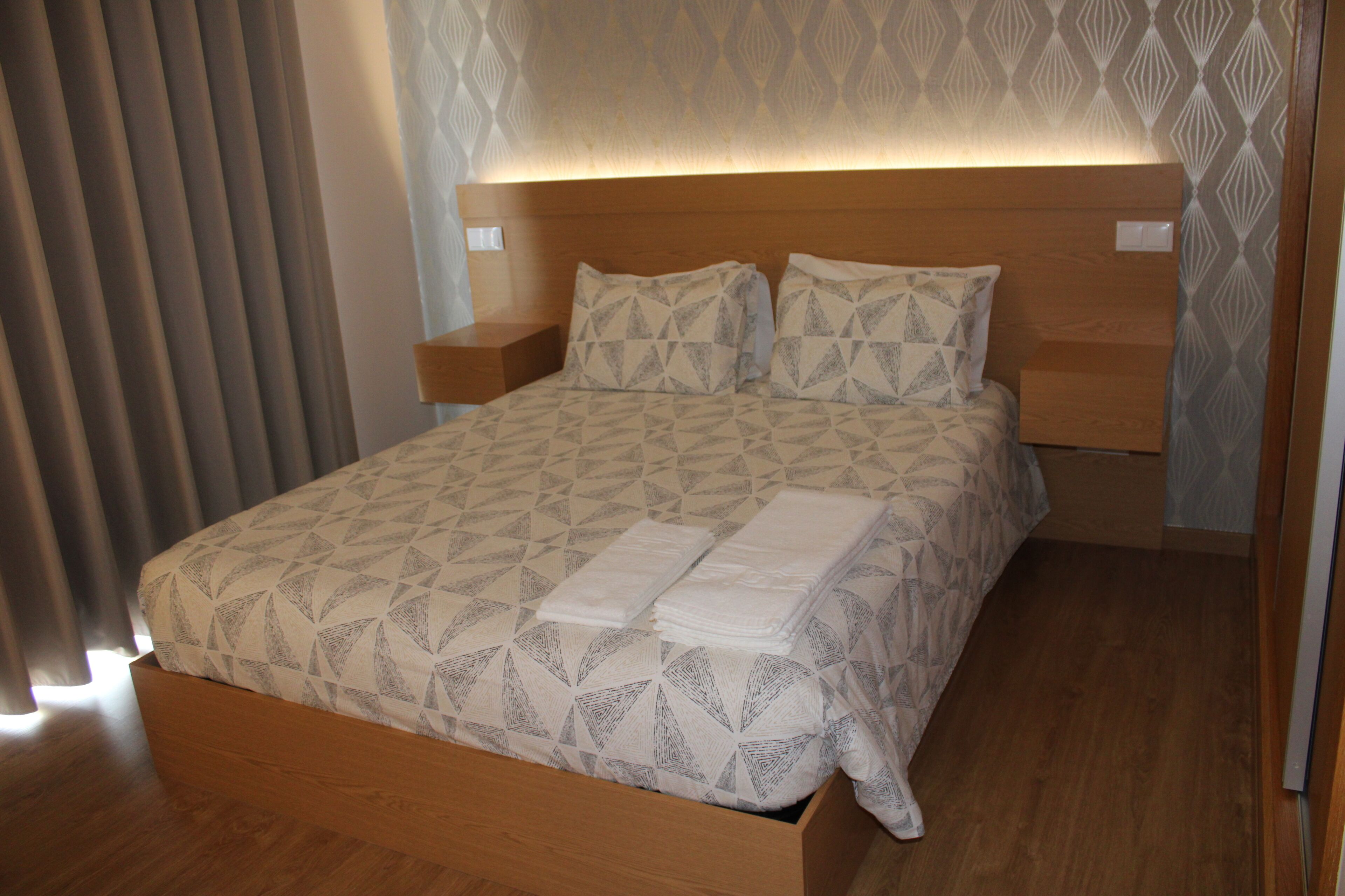 A neatly made bed with a geometric patterned bedspread and pillows, a wooden headboard, and bedside tables.