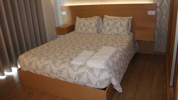 A neatly made bed with a geometric patterned bedspread and pillows, a wooden headboard, and bedside tables.