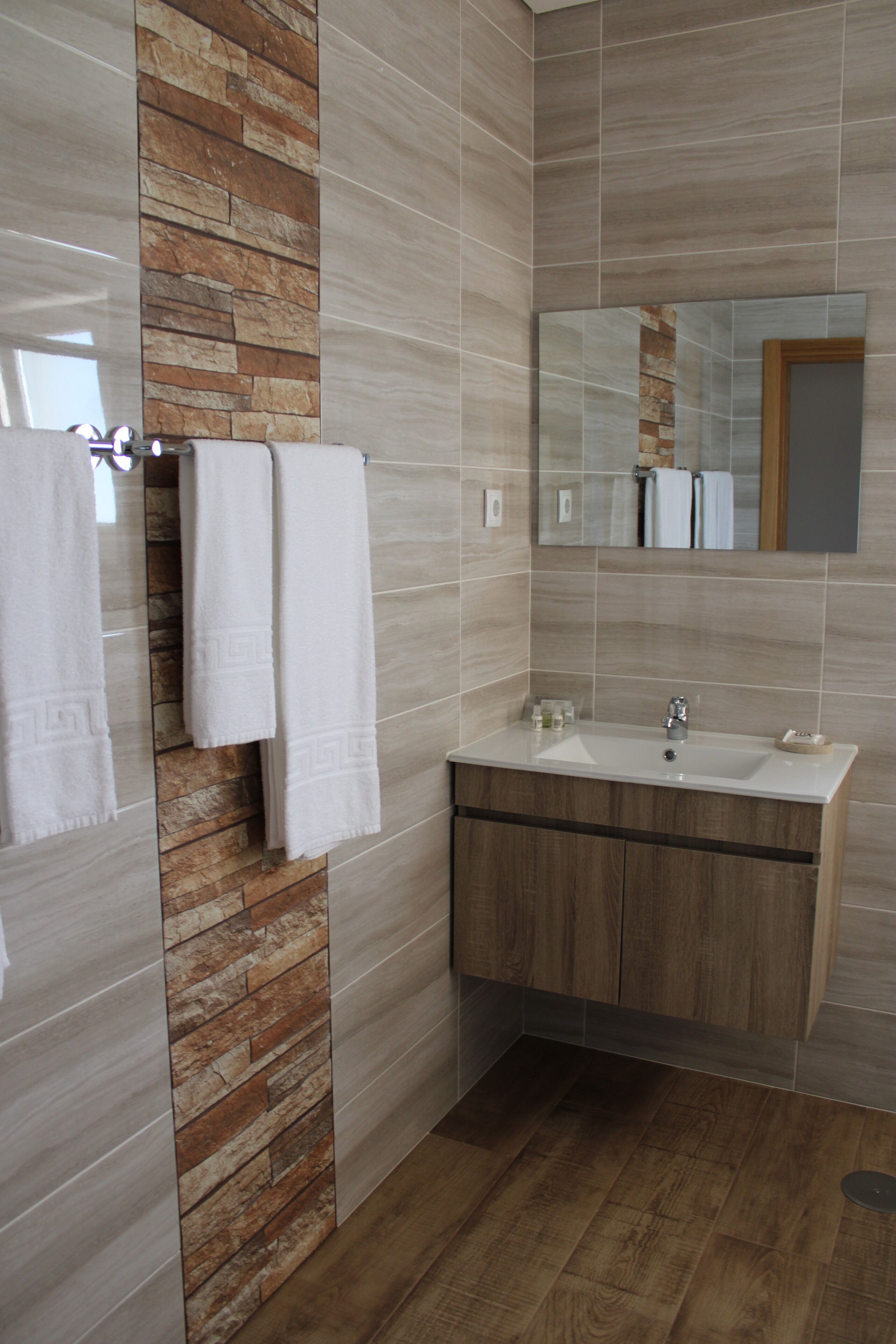 A bathroom with a stone accent wall, a wooden vanity, a mirror, and two white towels on a towel rack.