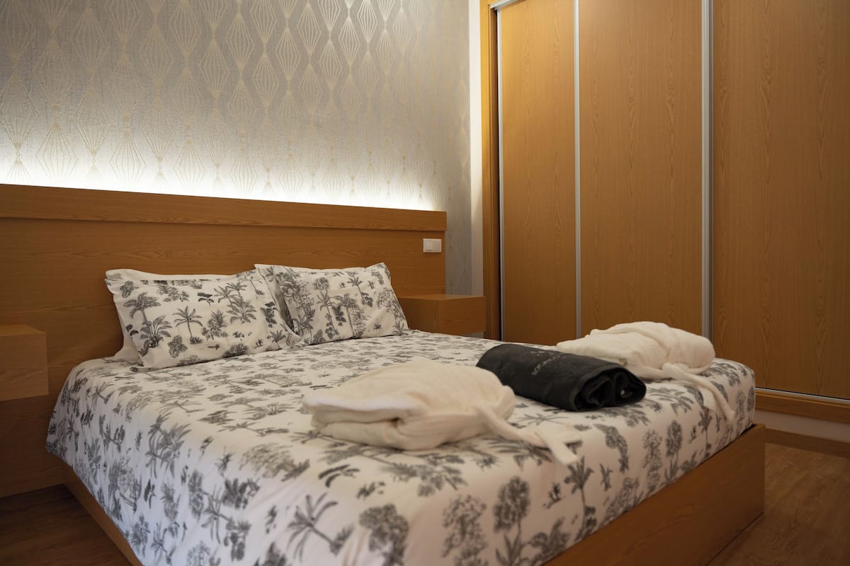 A neatly made bed with floral-patterned bedding, a bedside table, and a wardrobe.