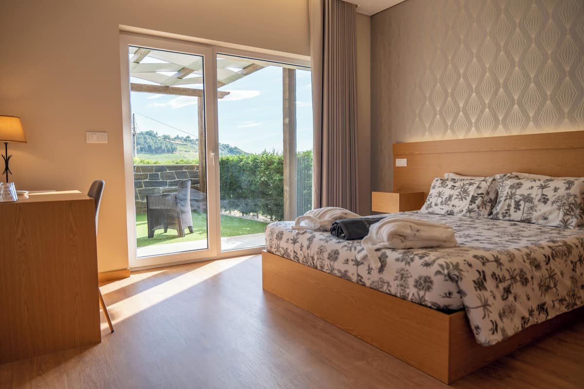 A bedroom with a bed, a desk, and a view of a garden through a sliding door.