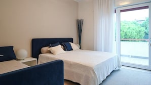 Hotellihuone, jossa on sänky, yöpöytä ja ikkunasta avautuva näkymä vehreään maisemaan.