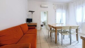 A room with a sofa, a dining table with chairs, a TV, and an air conditioning unit. - VILLA TERESA 02 (Lido di Jesolo)