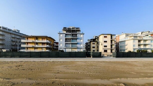 A multi-story residential building with balconies, a sandy ground in front, and a clear sky. - VILLA TERESA 02 (Lido di Jesolo)