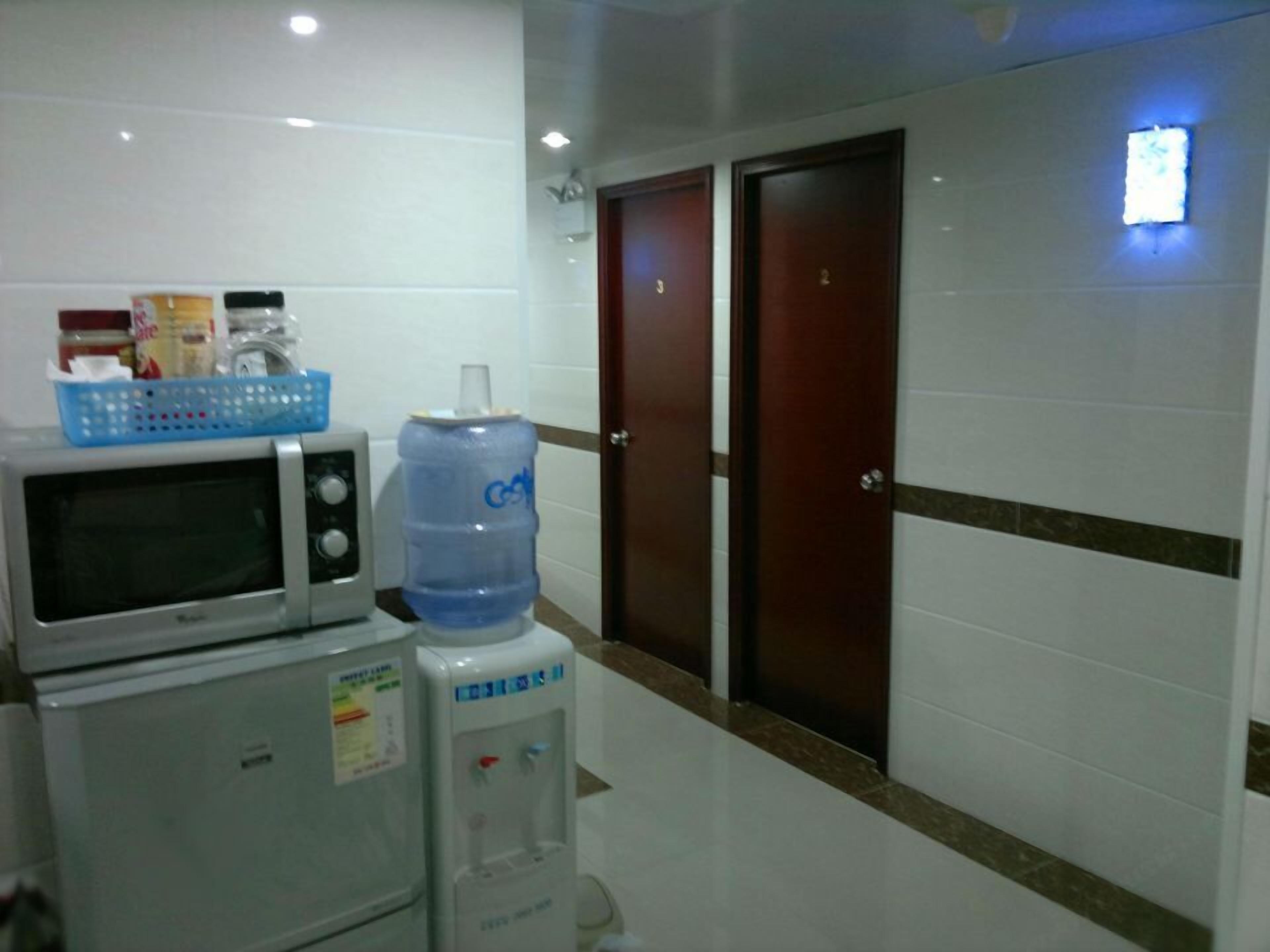 A kitchenette with a microwave, refrigerator, and water dispenser. There are two doors and a small window with a light.