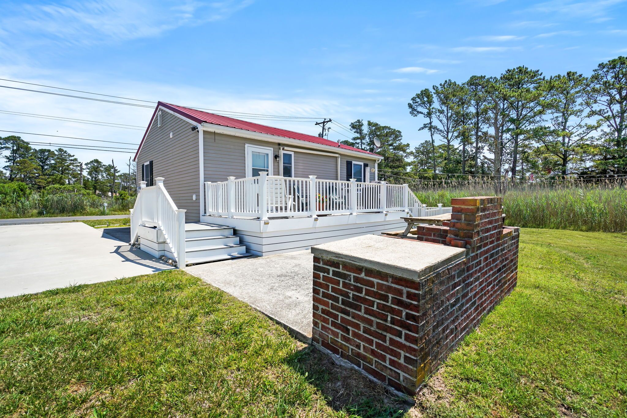 A single-story house with a red roof, white exterior, and a small porch with steps leading to a deck.