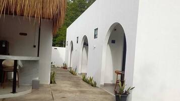 Un espace piscine agrémenté d’une structure à toit de chaume et de murs blancs percés d’arcades.