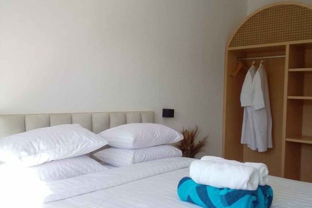 A neatly made bed with white linens and a stack of folded towels.