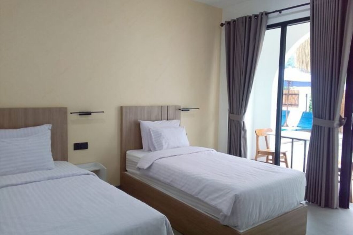 A hotel room with two beds, a wooden headboard, a small table, and a view of the outside.