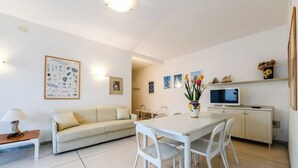 A modern living room with a white sofa, a dining table with chairs, a TV, and a cabinet. - VILLA TERESA 19 (Lido di Jesolo)