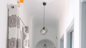 A hallway with a floral curtain, a red box, a mirror, and a hanging light fixture. - Seven Grapes - Karterados (Santorini)