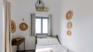 A bedroom with a bed, a desk, a window with curtains, and wall decorations. - Seven Grapes - Karterados (Santorini)