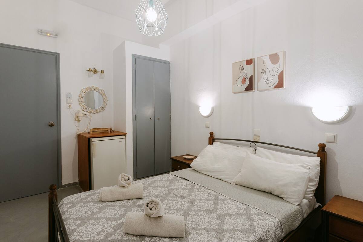 Une chambre à coucher comprenant un lit, des tables de chevet, une armoire, un miroir et des luminaires fixés au mur.