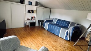 A cozy loft-style room with a wooden floor, a striped blue and white sofa, a white wardrobe, and a small table with books and a lamp.