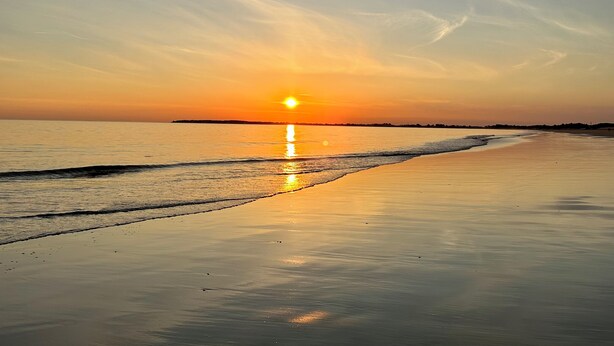 A beach at sunset with the sun reflecting on the water.