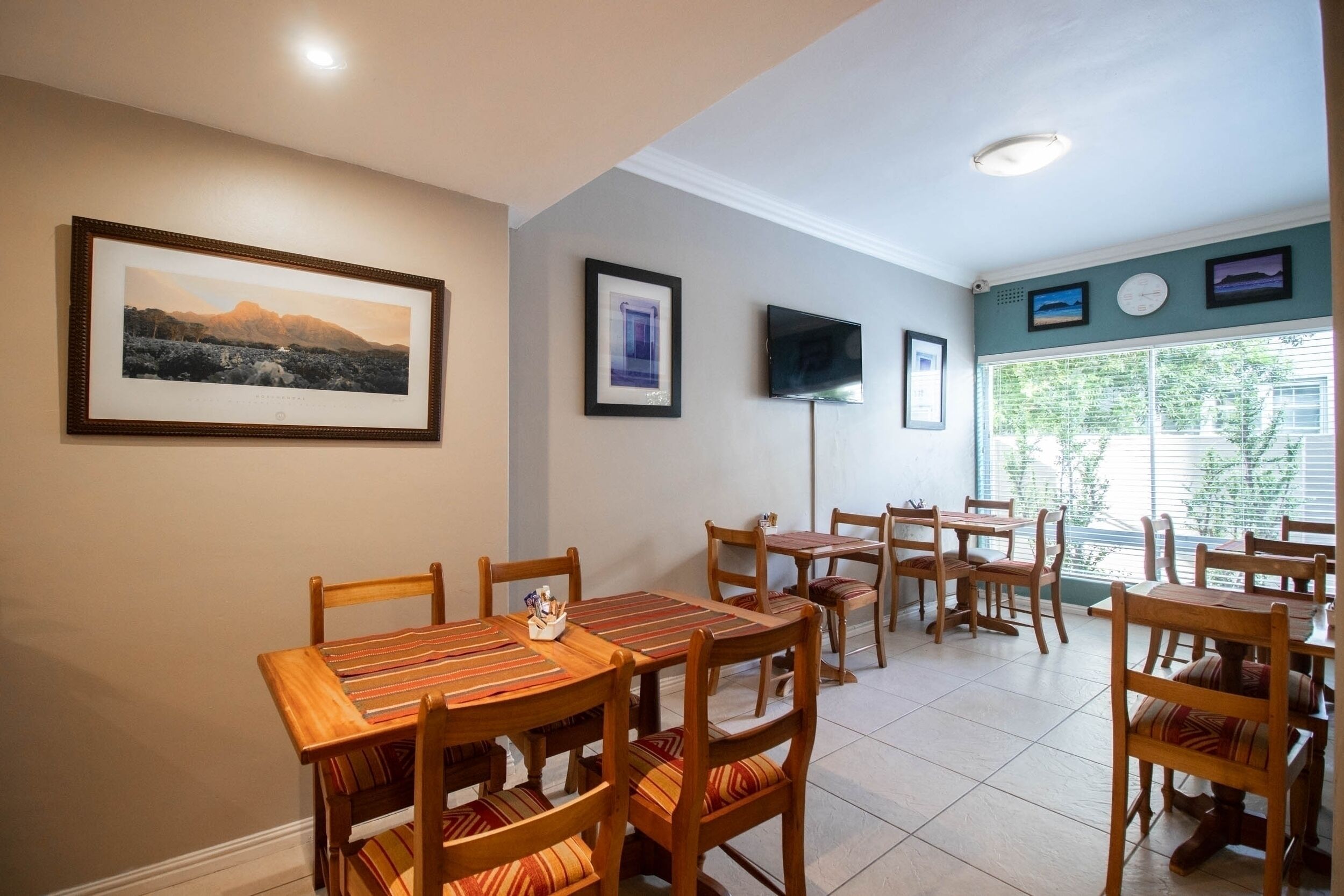 A dining area with wooden tables and chairs, framed pictures on the walls, and a television.