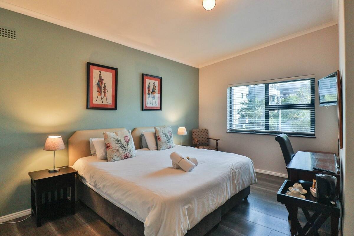 A neatly arranged bedroom with a bed, bedside lamps, a chair, and a window with blinds.